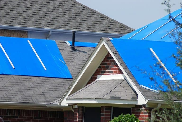 Storm damaged shingle roof protected by tarps before repair